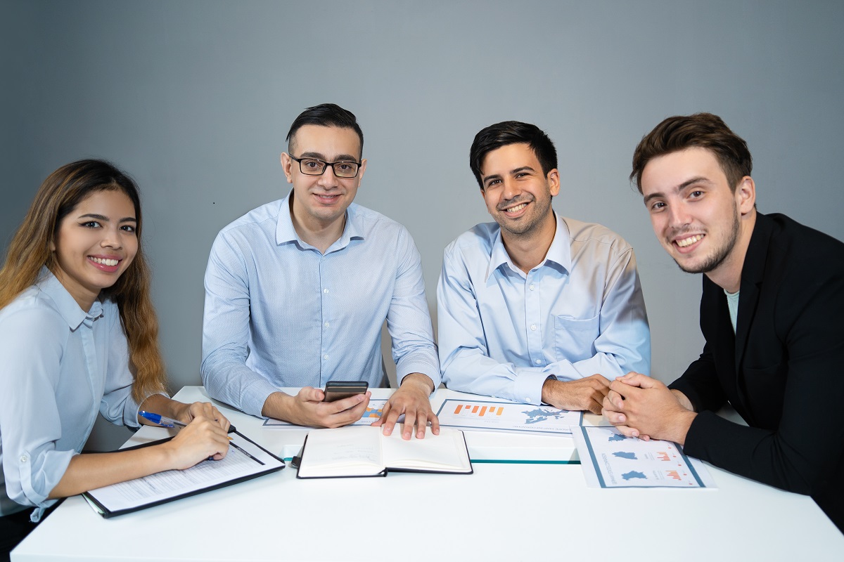 Portrait of happy business team sitting at table and smiling. Four young colleagues working with financial documents in office. Business team concept