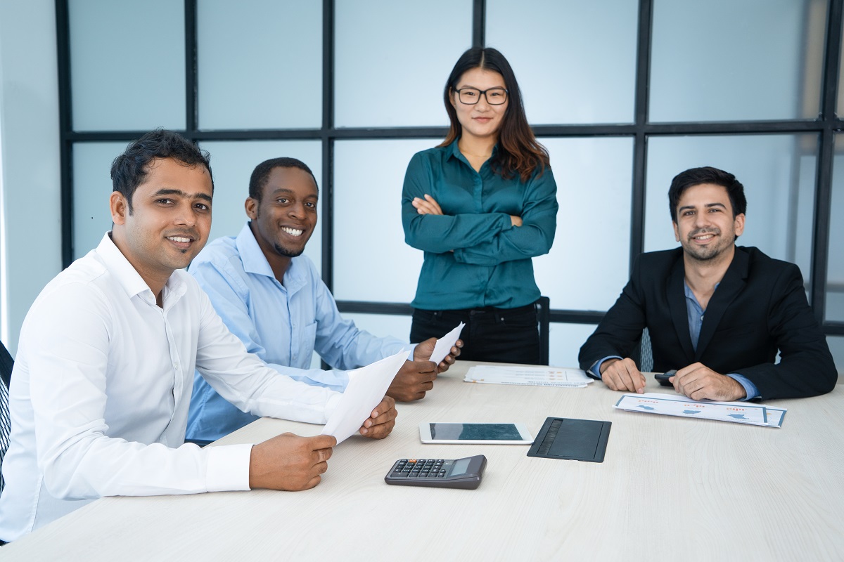 Positive successful international team holding business analysis at meeting. Confident pretty business lady proud of her team. Smiling managers looking at camera. Teamwork concept